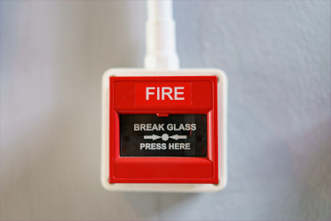 Photo of a fire alarm, displaying the 'Break glass. Press here' instruction