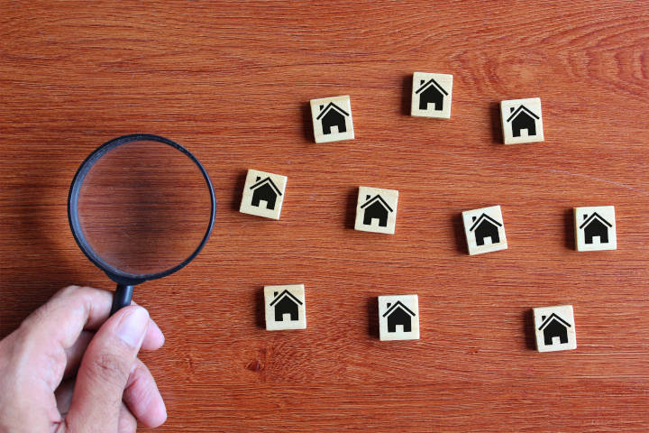 hand with magnifying glass looking at wooden block houses