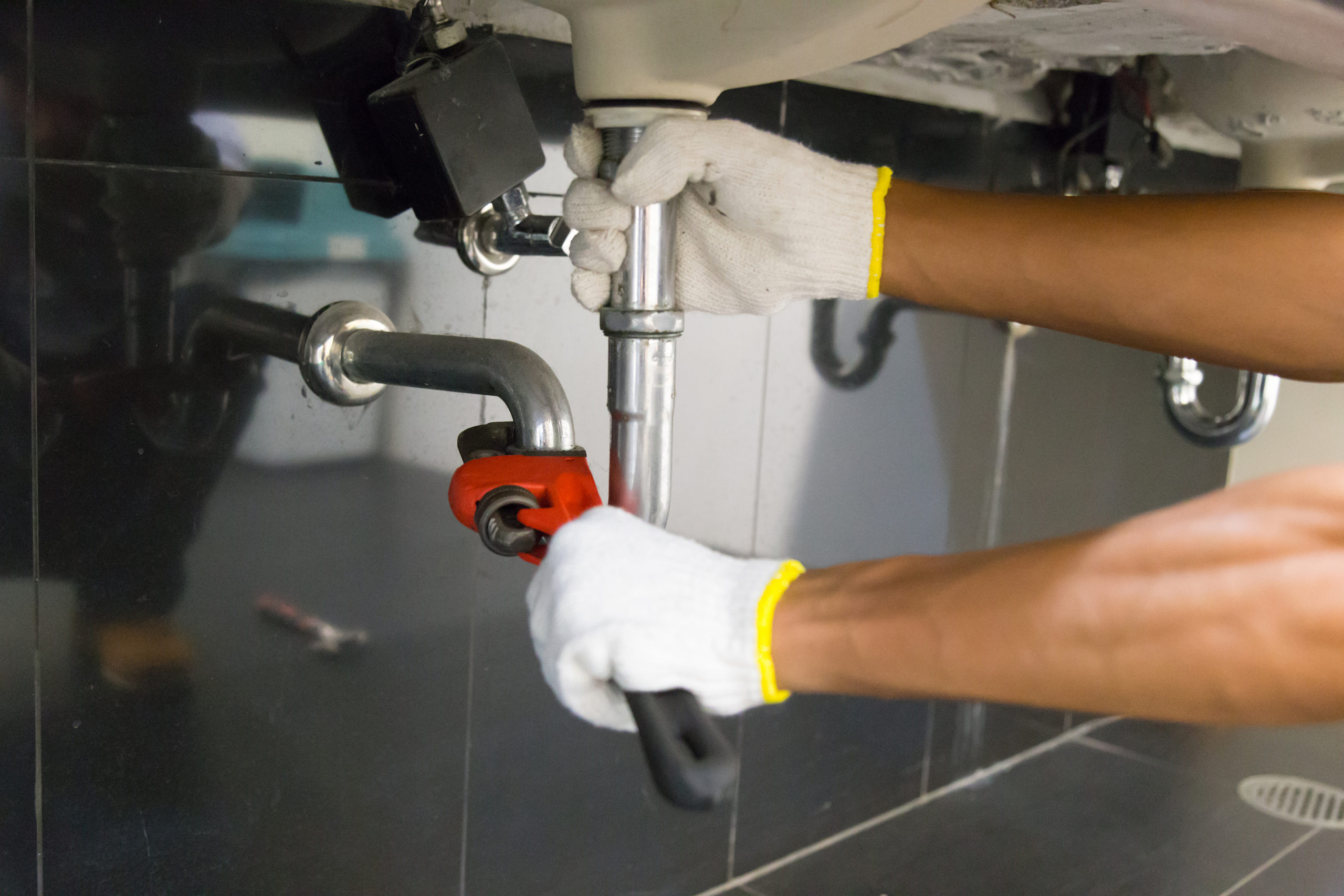 Plumber fixing white sink pipe with adjustable wrench.