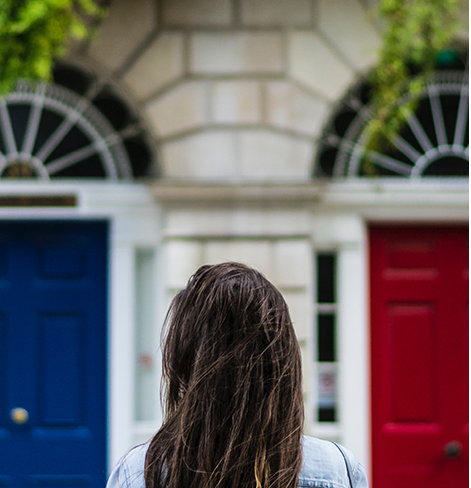 Photo showing the back of a brunette woman's head. The woman is standing in front of 2 doors, a blue and a red.