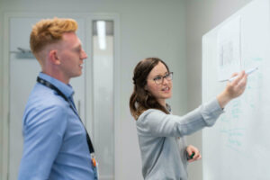 Two employees discussing a strategy on whiteboard in office space