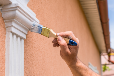 Photo of a man painting the outside details of his property,